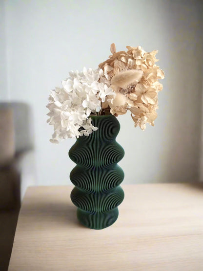 Green vase with white and beige dried flowers on a wooden surface.