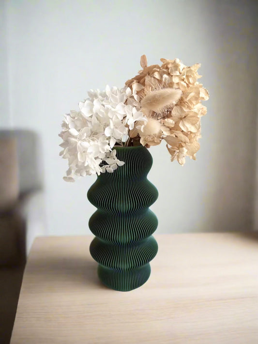 Green vase with white and beige dried flowers on a wooden surface.